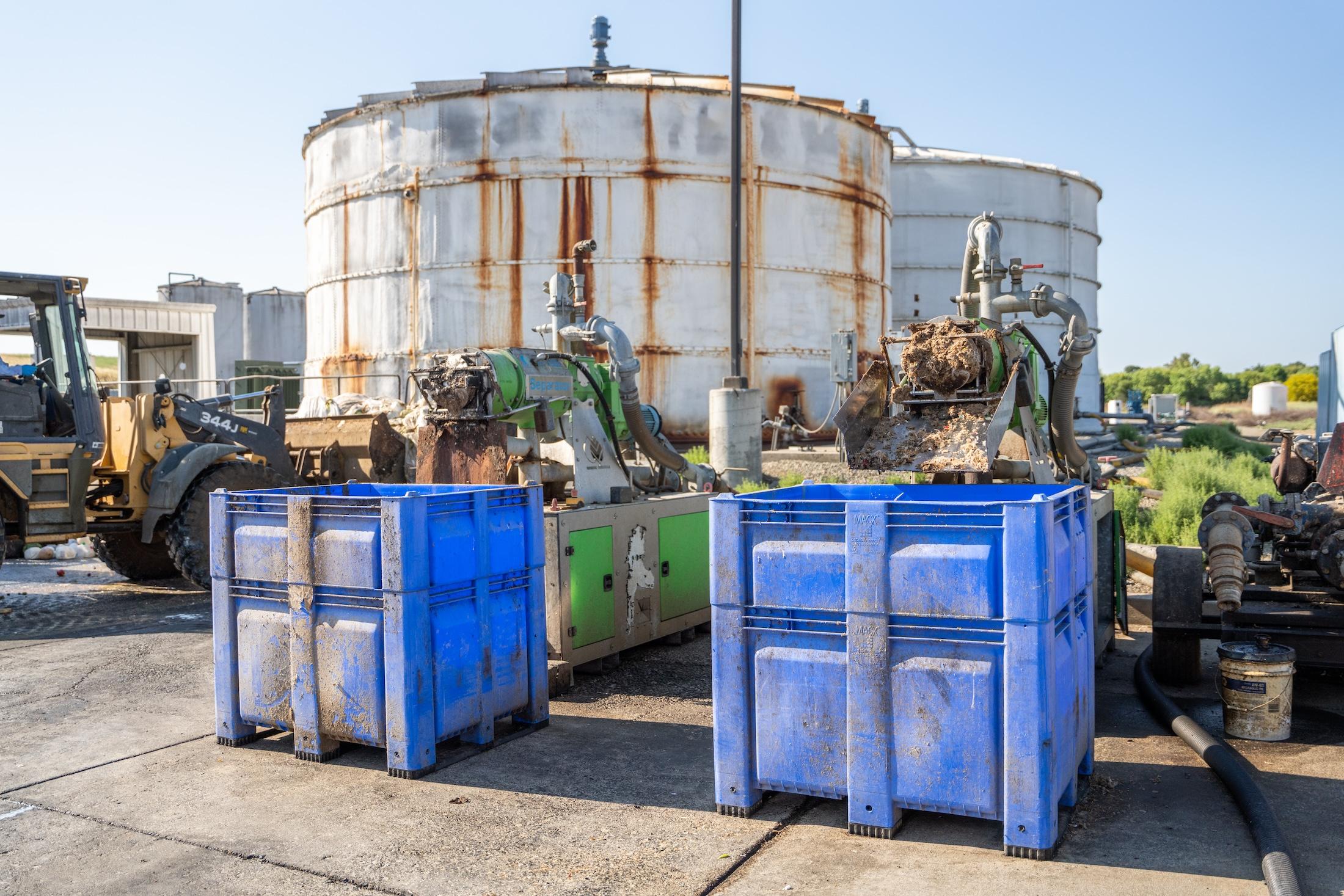 Two blue bins at the READ facility get filled with a sediment of organic waste and plastic from the digestion tank.