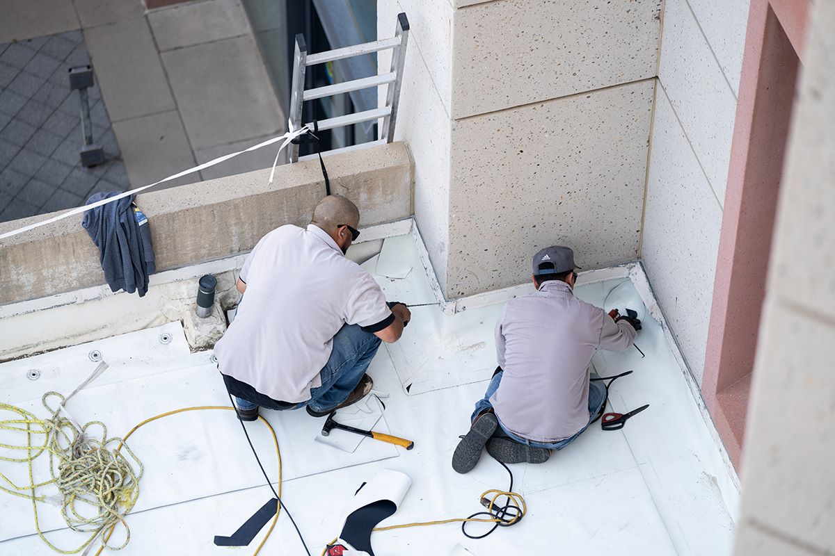 Image of two roofers laying down new material on the roof of a building at UC Davis.