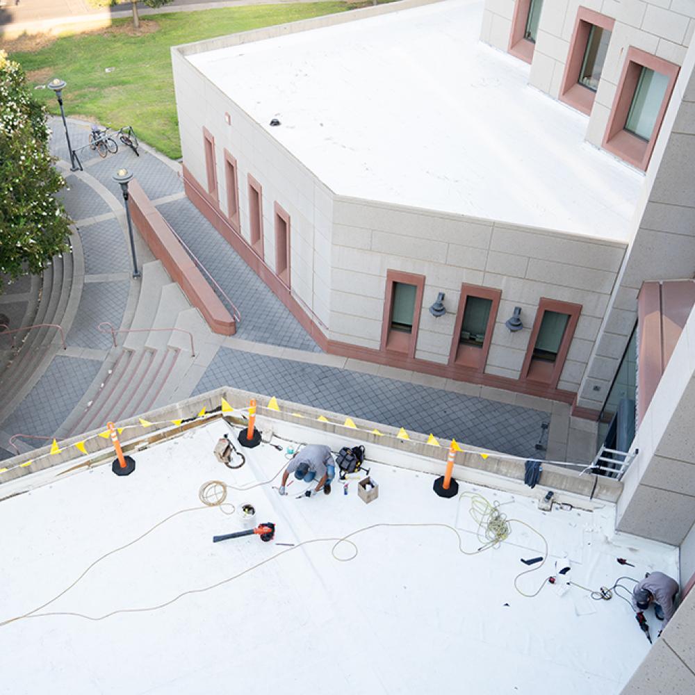 Image from far above roof workers repairing a roof on the UC Davis campus.