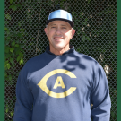 Smiling man in navy hoodie with yellow A logo and white-blue cap in front of chain-link fence